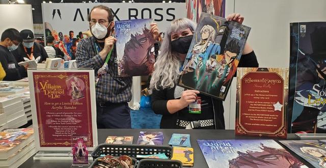 Two masked people holding up posters in front of some small baskets with pins