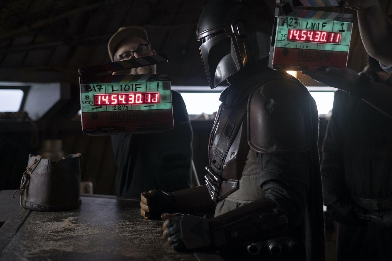 Set Still of The Mandalorian standing at a bar, directors are behind him holding clapperboards