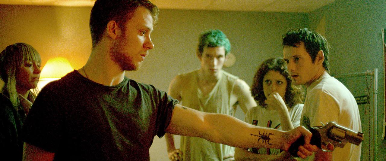 Still image from Green Room, Joe Cole points a gun at offscreen figure, Anton Yelchin in background