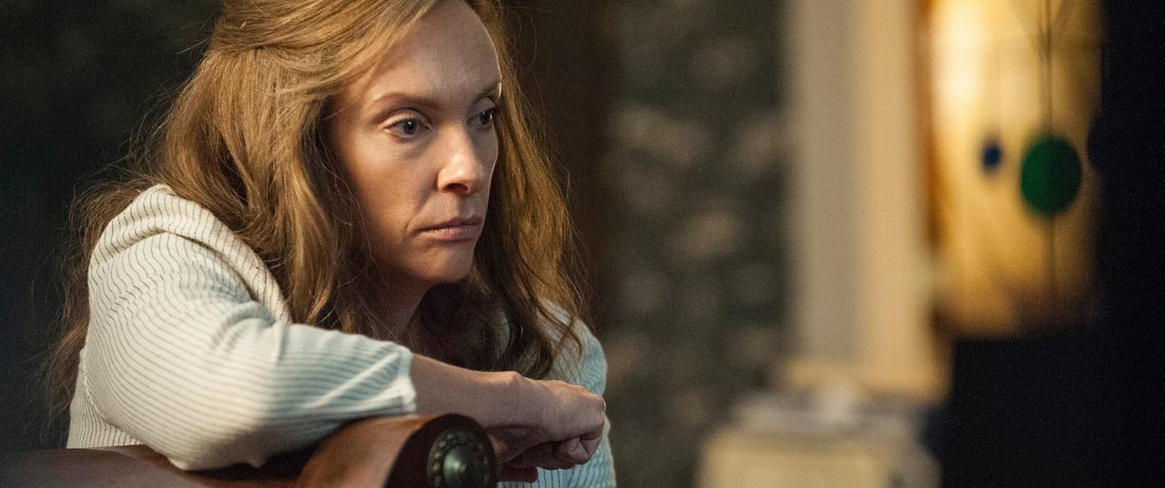 Still image from Hereditary. Toni Collette leans against a piece of furniture.