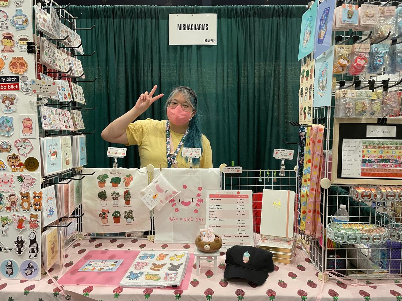 Image of artist throwing up peace sign behind their display