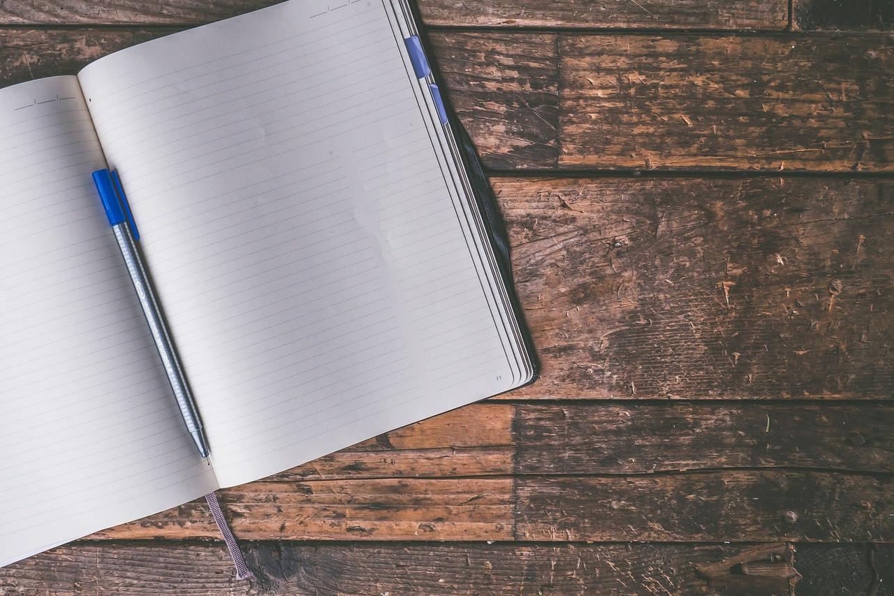 Photograph of an open notebook and blue pen on a dark wood desk