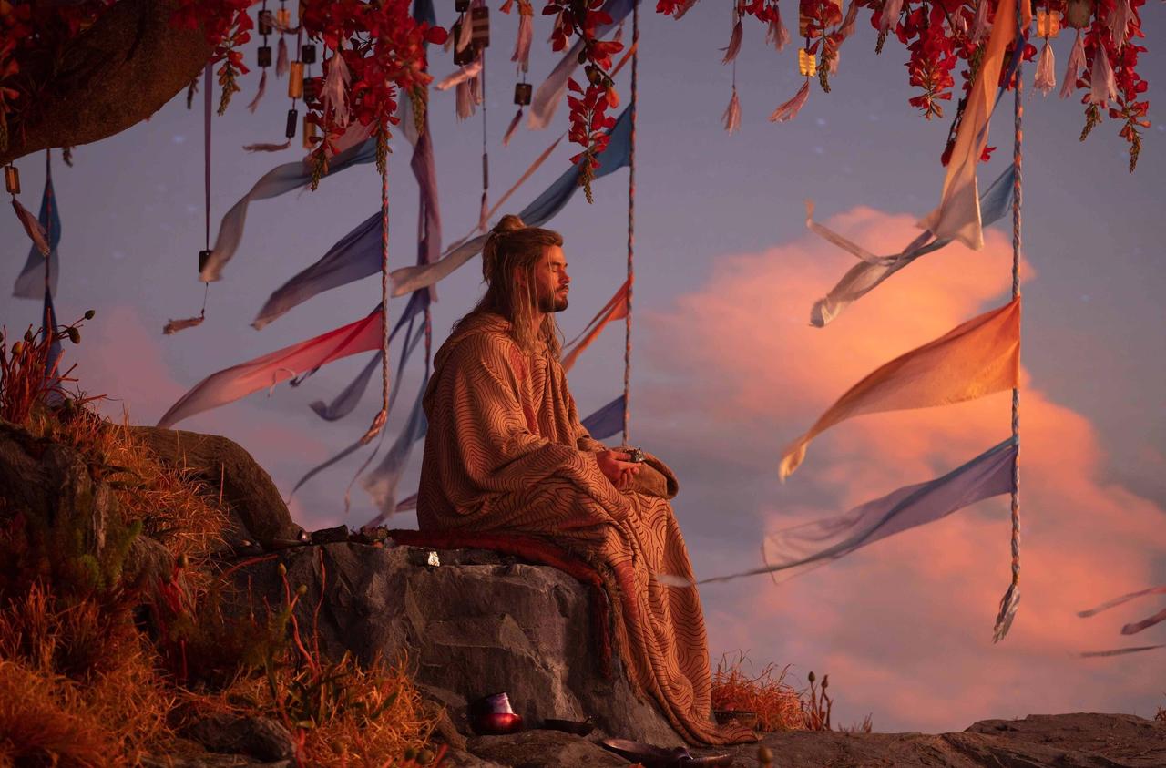 Still from Thor Love and Thunder, Chris Hemsworth as Thor is sitting on a rock under a tree wearing long robes